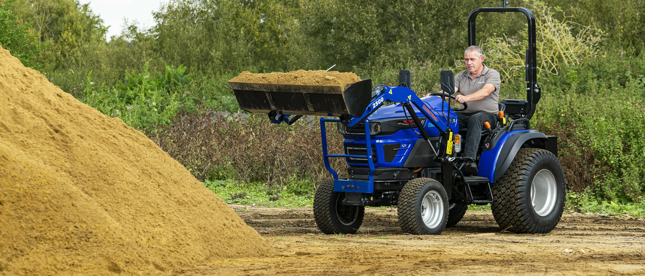 The Farmtrac FT25G being used to transport sand in a front-loader attachment.